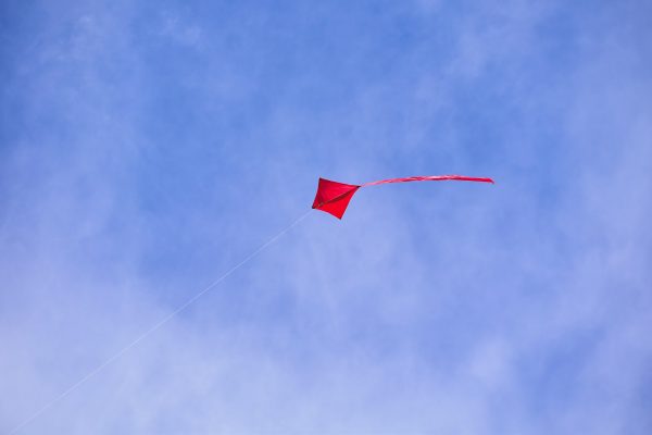Κόκκινος χαρταετός πετάει στον γαλανό ουρανό, ακολουθώντας τις οδηγίες του ΑΔΜΗΕ για ασφαλές πέταγμα.