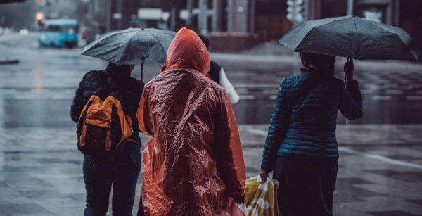 Άνθρωποι με ομπρέλες και αδιάβροχα περπατούν στον δρόμο κάτω από βροχή, ενόψει του καιρού που έρχεται.