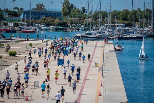 Δρομείς συμμετέχουν στον 16ο Ποσειδώνιο Ημιμαραθώνιο στο Φλοίσβο, με φόντο τη θάλασσα και τα σκάφη.