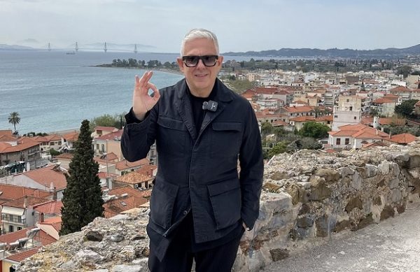 Ο Τάσος Δούσης με το σήμα ΟΚ μπροστά από την όμορφη Ναυπακτία και τη γέφυρα Ρίου-Αντιρρίου.