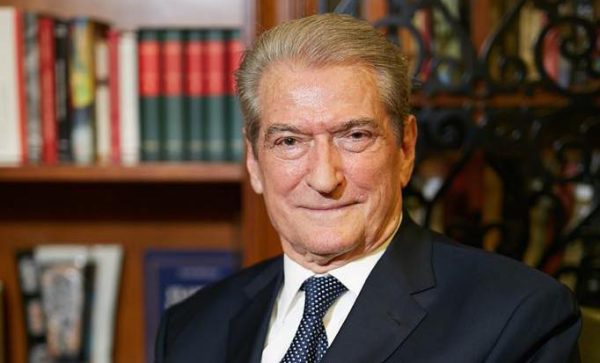 Ο Μπερίσα ποζάρει χαμογελαστός μπροστά από ράφια με βιβλία, δείχνοντας αλλαγή τροπαρίου.