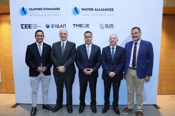 Πέντε άνδρες ποζάρουν μπροστά από πανό με λογότυπα για τις «Υδάτινες Συμμαχίες» και την ευαισθητοποίηση για τη λειψυδρία.