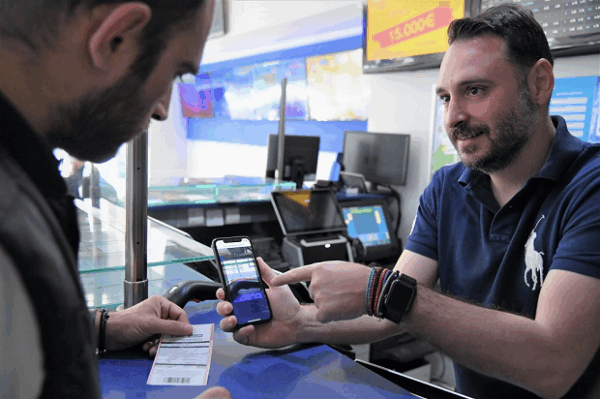 Υπάλληλος καταστήματος ΟΠΑΠ δείχνει την οθόνη του κινητού για το πρόγραμμα εξέλιξης και επιβράβευσης Level Up.