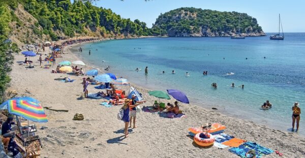 Οργανωμένη παραλία με κόσμο να απολαμβάνει τις διακοπές του κάτω από ομπρέλες και να κολυμπά στα γαλάζια νερά.