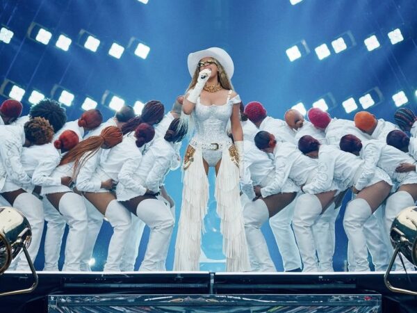 Η Beyoncé με λευκό σύνολο και καουμπόικο καπέλο στη σκηνή της Cowboy Carter Tour, πλαισιωμένη από χορευτές.