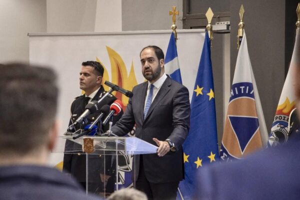 Ο υπουργός Κεφαλογιάννης μιλά σε δημοσιογράφους με σημαίες της Ελλάδας και της ΕΕ στο παρασκήνιο.