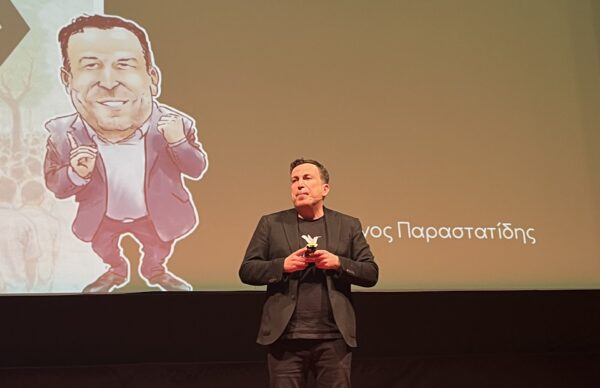Ο Ντέμοκρατ, Στέφανος Παραστατίδης, μιλάει για την πολιτική και τη δημοκρατία, με μια καρικατούρα του στο πλάι.
