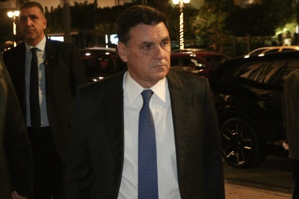 Ο Άγγελος Φιλιππίδης με κοστούμι και γραβάτα, σε νυχτερινή έξοδο, με αυτοκίνητα στο φόντο.