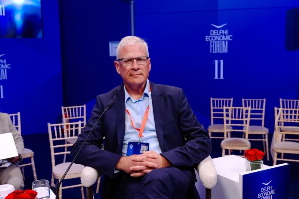 Άνδρας με γυαλιά και μπλε κοστούμι σε συνέδριο του Delphi Economic Forum, συζητώντας για πυροσβεστικά αεροσκάφη.