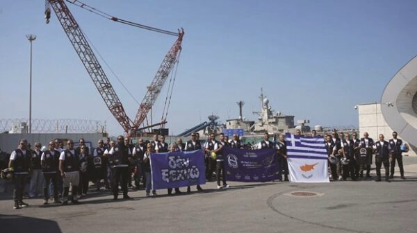 Συμμετέχοντες στις μοτοπορείες στη μνήμη Ισαάκ – Σολωμού κρατούν σημαίες και πανό μπροστά από πλοίο και γερανούς.