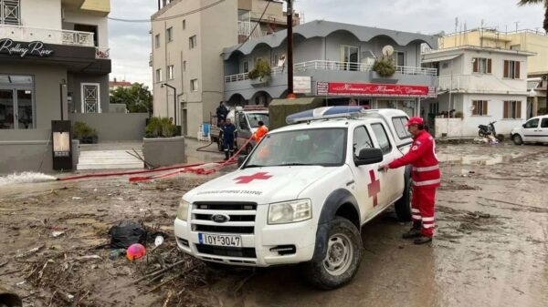 Εθελοντής του Ελληνικού Ερυθρού Σταυρού στέκεται δίπλα σε όχημα κατά τη διάρκεια πλημμυρικών φαινομένων.