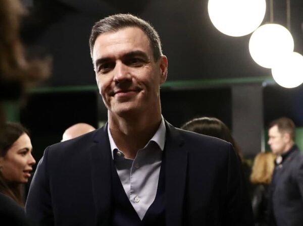 Πολιτικός χαμογελάει σε εσωτερικό χώρο, με άλλους ανθρώπους στο παρασκήνιο, κατά τη διάρκεια της στεγαστικής κρίσης στην Ισπανία.