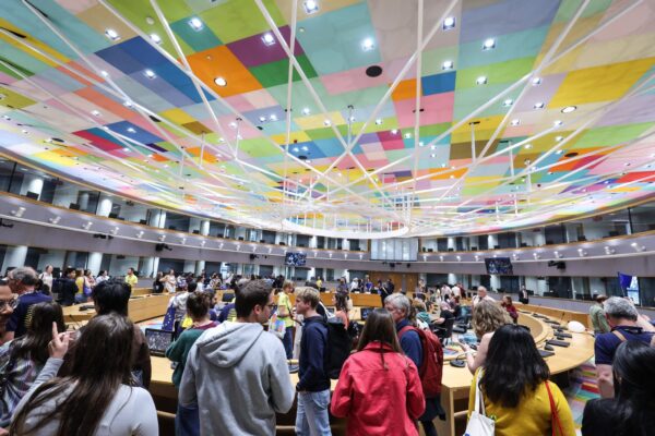 Συνάντηση στο Ευρωπαϊκό Συμβούλιο με πολύχρωμη οροφή και πλήθος κόσμου να συζητά για μέτρα α λα καρτ στην ενέργεια.